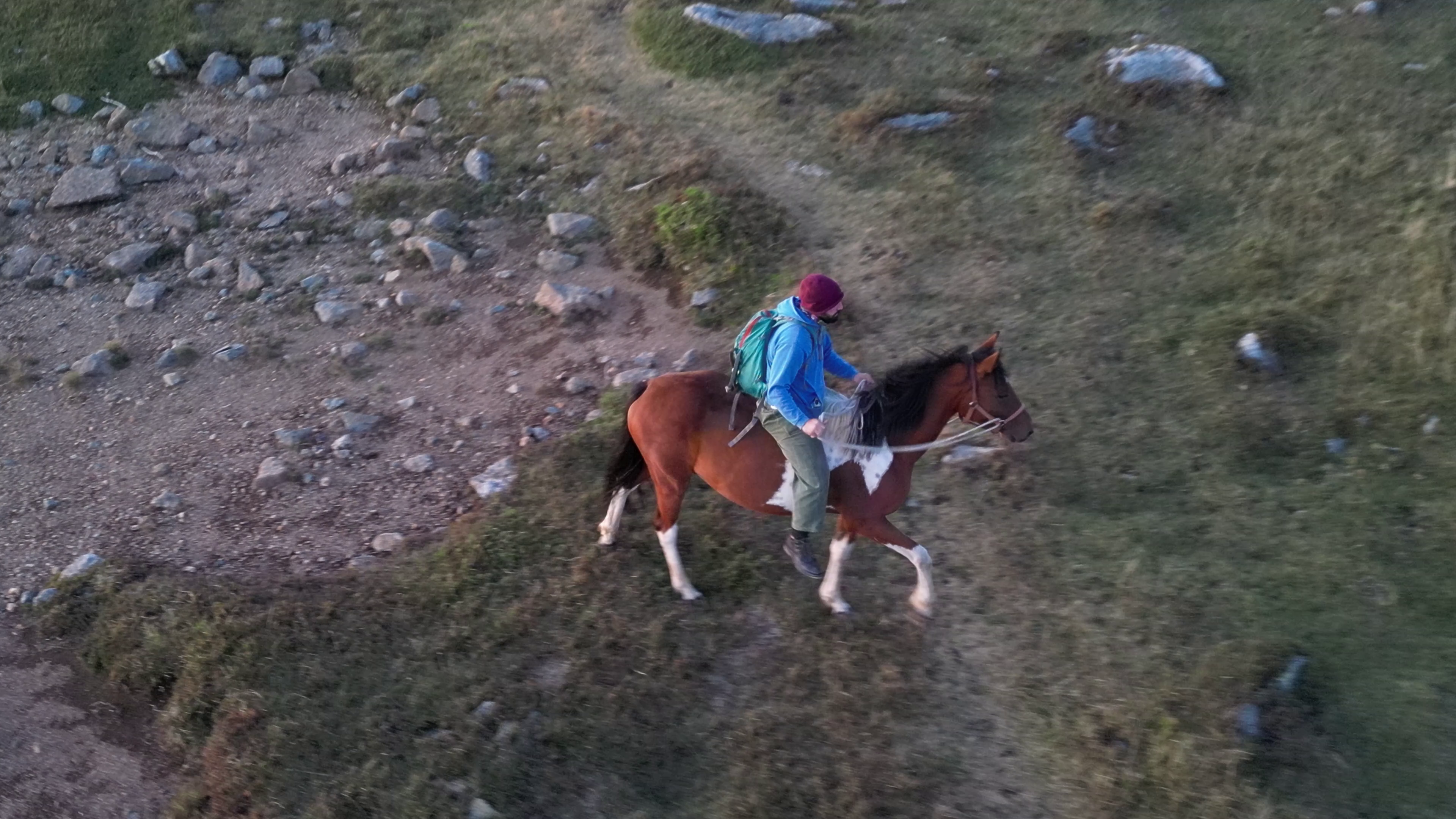 An image of a man on a horse crossing an animal track on rocky terrain